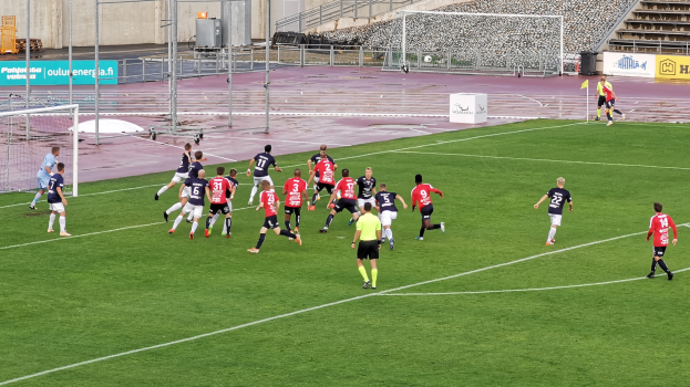 Gruppe junger Frauen, die Fußball auf einem Rasenfeld mit Maschendrahtzaun und einer Wand im Hintergrund spielen, mit der Beschriftung "Paris Saint-Germain Frauenfußball" in der rechten unteren Ecke.