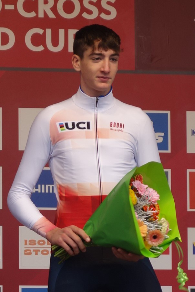 Ein Mann steht auf einem Podium und hält einen Blumenstrauß in der Hand, feiernd mit einem selbstbewussten und stolzen Gesichtsausdruck.