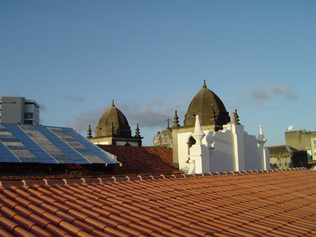 Eine Stadtansicht mit Gebäuden im Vordergrund, einem klaren blauen Himmel im Hintergrund und Solarpanelen auf dem Dach eines der Gebäude.
