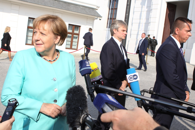 Bundeskanzlerin Angela Merkel spricht vor dem Kanzleramt in Berlin zu Reportern, umgeben von einer Gruppe von Menschen, einige halten Mikrofone, mit Gebäuden im Hintergrund.