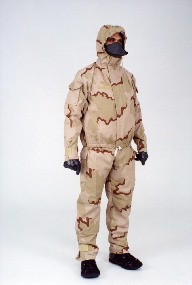 Mann in einem Tarnmuster-Schutzoverall mit Kapuze und Maske vor einem weißen Hintergrund.