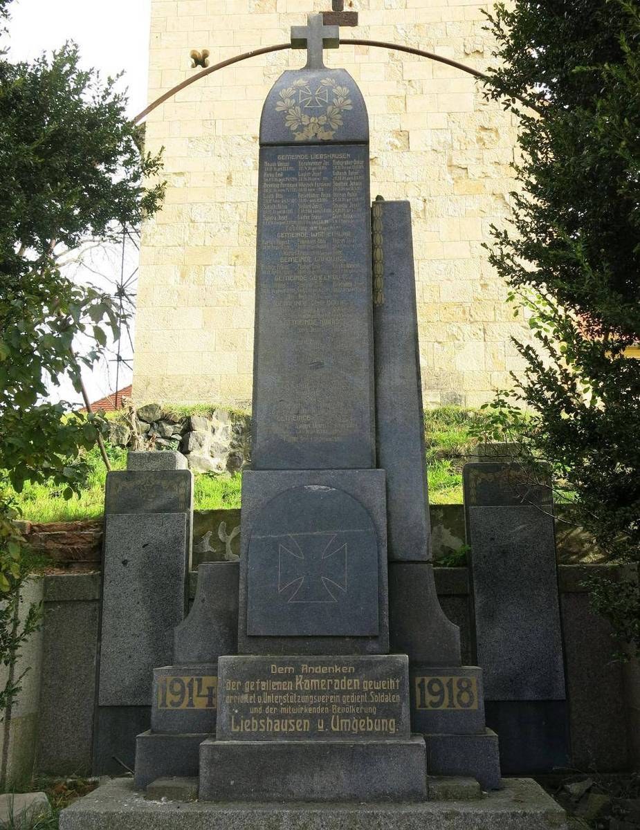 Denkmal vor einer Kirche mit einem Kreuz, umgeben von Bäumen und einer Mauer, gewidmet deutschen Soldaten, die im Zweiten Weltkrieg starben.