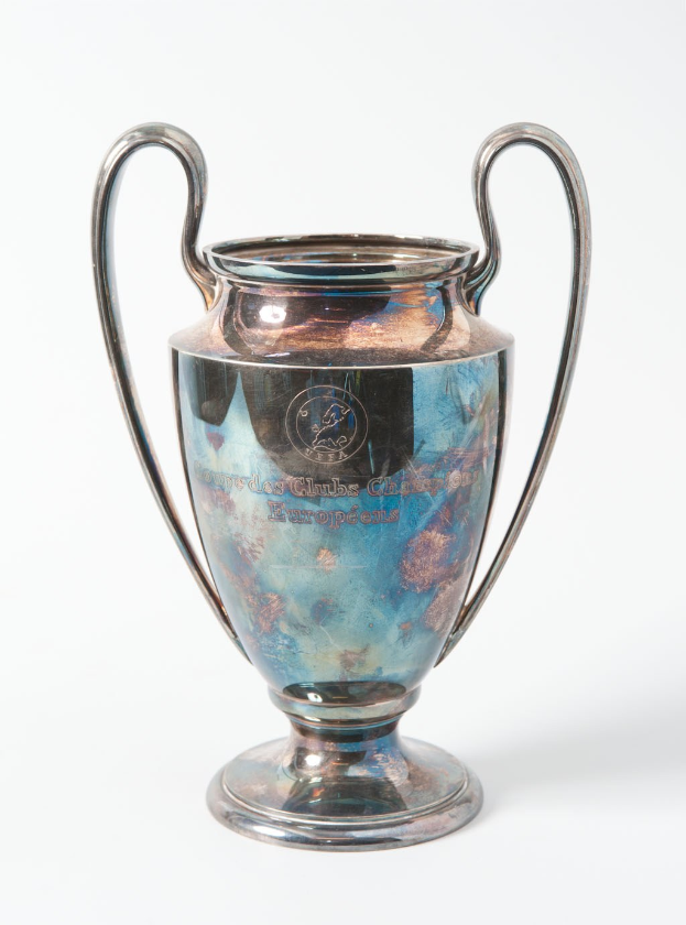 Der UEFA-Champions-League-Pokal, ein stählerner Becher mit zwei Griffen und einem blauen und silbernen Farbschema, mit der Inschrift "UEFA Champions League", vor einem weißen Hintergrund dargestellt.