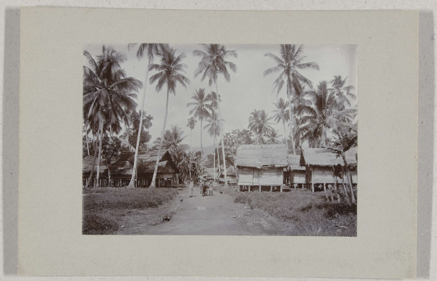 Schwarzes und weißes Rahmenfoto eines Dorfes mit Hütten, Menschen und Palmen.