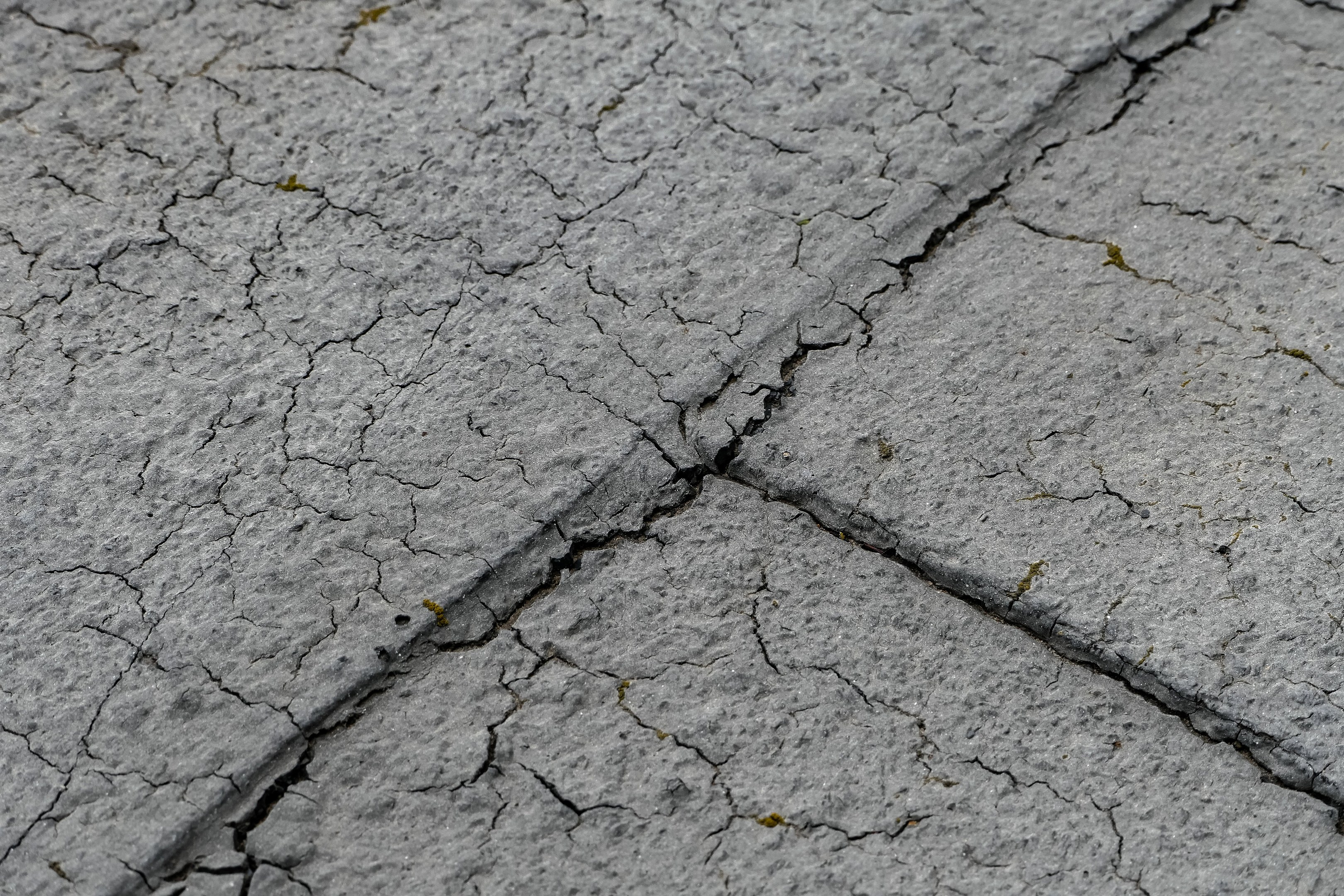 Nahaufnahme einer gebrochenen, verwitterten Straßenoberfläche mit tiefen, breiten Rissen und einer unebenen, rauen Textur.