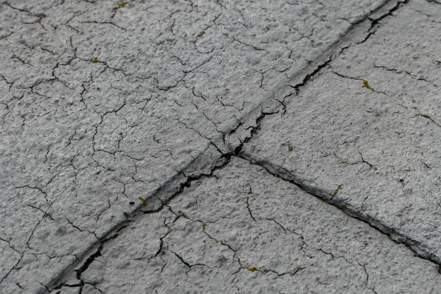 Nahaufnahme einer gebrochenen, verwitterten Straßenoberfläche mit tiefen, breiten Rissen und einer unebenen, rauen Textur.