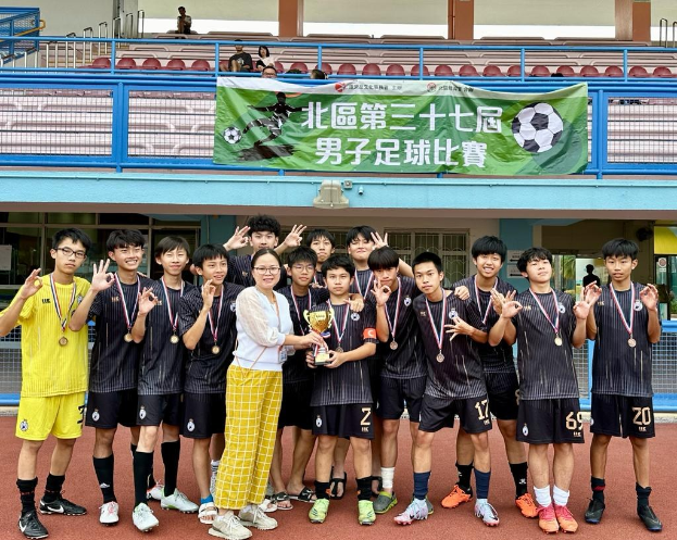 Gruppe junger Männer in Fußballtrikots auf einem Feld mit einem Pokal und Medaillen stehend, im Hintergrund ein Banner mit der Aufschrift 'Yokohama U-16 Jungenfußballteam'