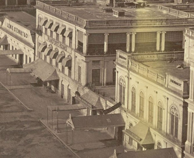 Altes Schwarz-Weiß-Foto einer Stadtstraße mit Gebäuden, Fenstern, Säulen, Namensschildern, Schuppen und Pfählen.