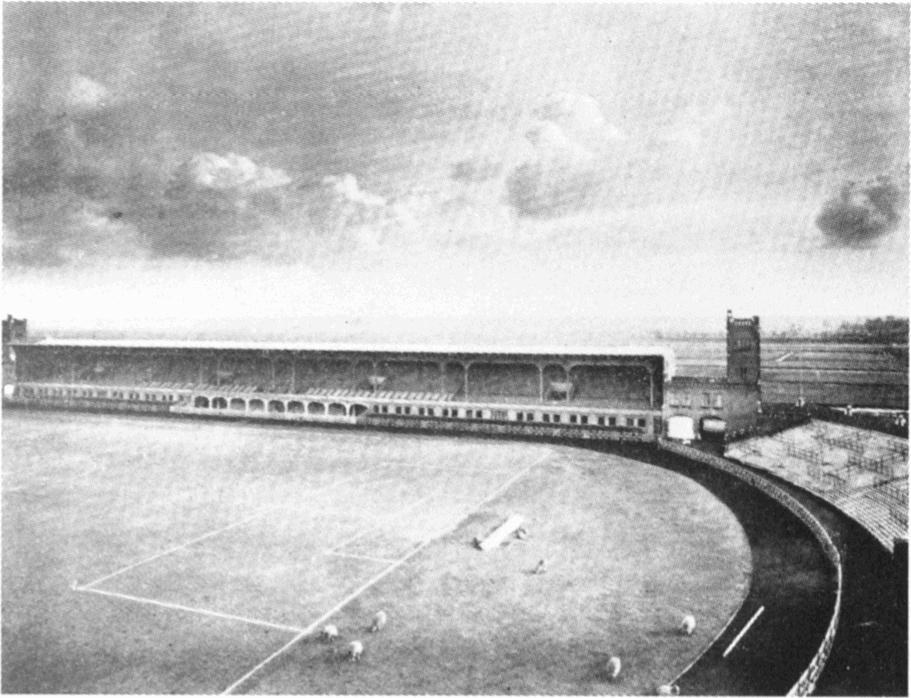 Ein Schwarz-Weiß-Foto eines Fußballfeldes mit einem Stadion, das von Bäumen umgeben ist und von einer bewölkten Himmel
