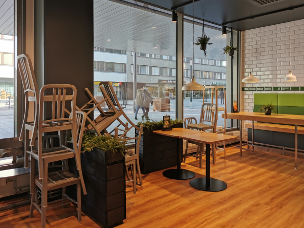 Ein Berliner Restaurant mit Holztischen und -stühlen in der Nähe eines großen Fensters, das Fußgänger, Gebäude und Straßenelemente zeigt.
