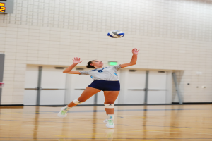 Eine weibliche Volleyballspielerin in Sneakers springt, um den Ball in der Luft zu treffen, mit einer Wand und Türen im Hintergrund.
