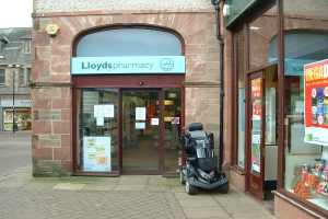 Eine Apothekenfiliale mit einem vor dem Gebäude geparkten Fahrzeug und einem Gebäude auf der linken Seite.