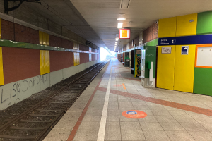 Ein Bahnhof in Berlin, Deutschland, mit einem Zug auf den Schienen, beleuchteter Deckenbeleuchtung, Graffiti an der linken Wand und ein paar Gegenständen auf der rechten Seite.