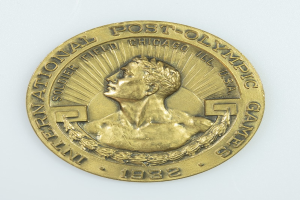 Eine Goldmedaille mit der Inschrift "Internationale Post-Olympische Spiele" auf einem weißen Hintergrund.