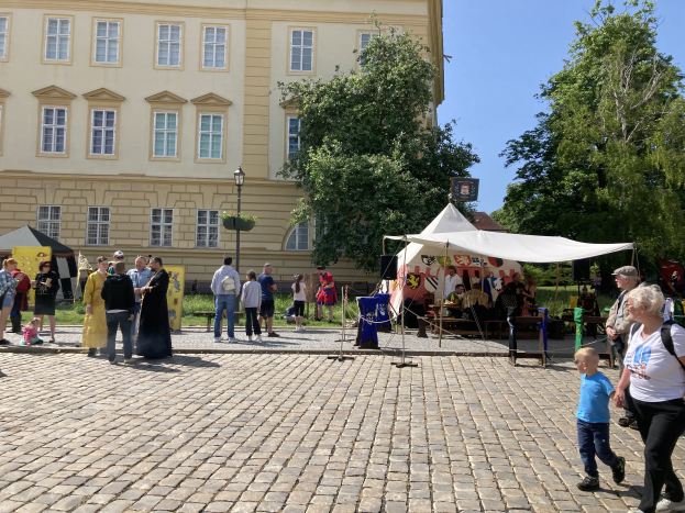 Eine Gruppe von Menschen geht eine Kopfsteinpflasterstraße in Krakau, Polen, entlang, mit Zelten, Tischen und Bäumen an der Straße und einem Gebäude mit sichtbarem Text im Hintergrund.