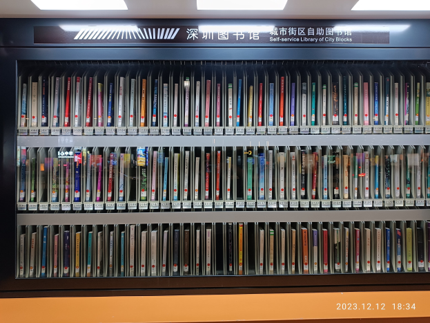 Eine gut beleuchtete Bibliothek mit hohen Bücherregalen voller Bücher, mit einer Tafel mit Text und einem Wasserzeichen unten, ähnlich einer Selbstbedienungsbibliothek der Stadtblöcke.