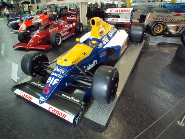 Eine Gruppe von Rennwagen in einem Museum ausgestellt, umgeben von Menschen