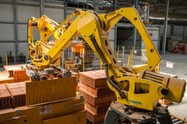 Ein großes Lager voller numerous boxes, Kräne, einen Zaun, Pfosten und andere industrielle Ausrüstung, mit einer Wand im Hintergrund, die auf eine größere industrielle Umgebung hinweist.