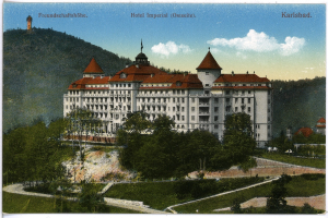 Eine alte Postkarte zeigt das Hotel Imperial in Karlsbad, Deutschland, ein großes Gebäude mit vielen Fenstern, umgeben von Bäumen, Pflanzen und Gras, mit einem Weg, einer Baumgruppe, Hügeln und einem bewölkten Himmel im Hintergrund und Text oben.
