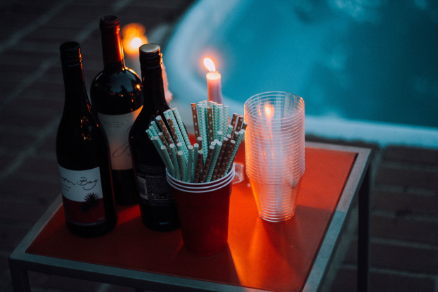 Ein Tisch am Swimmingpool mit zwei Weinflaschen, einer brennenden Kerze, Gläsern und Strohhalmen, der eine Vorbereitung für eine entspannte Nacht im Freien vermuten lässt.