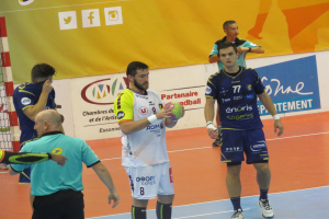 Eine Gruppe von Männern steht auf einem Futsal-Platz, einer hält einen Ball, daneben ein Tor und im Hintergrund Banner.