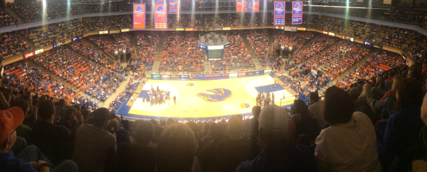 Eine große Arena voller Zuschauer, die ein Basketballspiel beobachten, mit Spielern auf dem Feld, sitzenden Fans in den Rängen und Lichtern und Bannern oben.