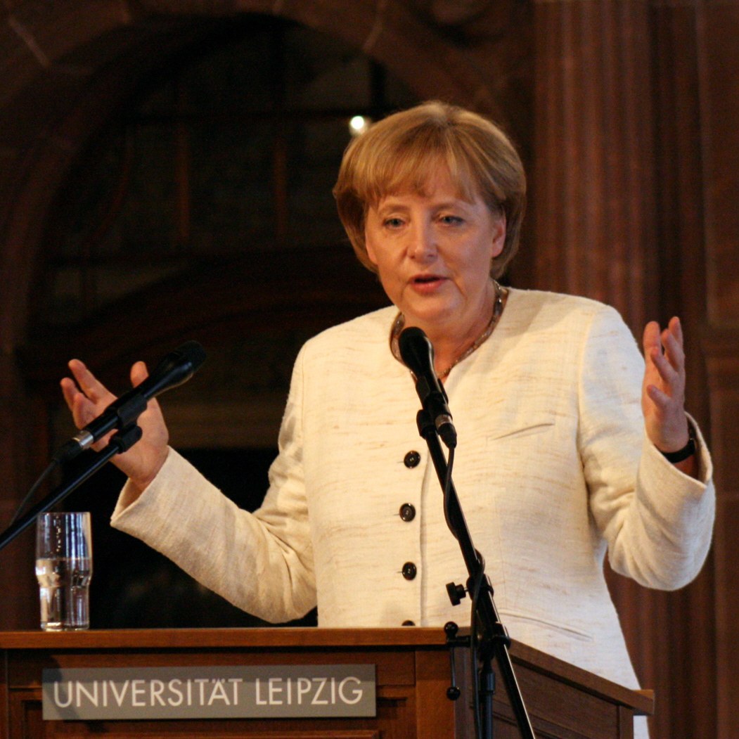 Bundeskanzlerin Angela Merkel hält eine Rede an einem Rednerpult mit einem Mikrofon und einem Glas Wasser an der Universität Leipzig.