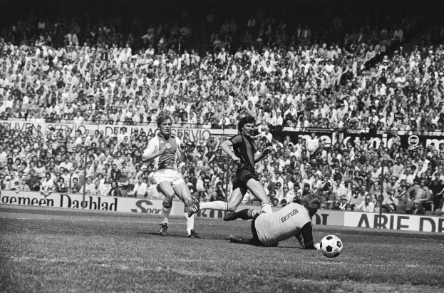 Schwarzes Foto von Männern, die Fußball auf einem Feld mit Zuschauern im Hintergrund und einem Banner "Bundesliga 1978-79 Ajax 1-1 Hannover 96" spielen.