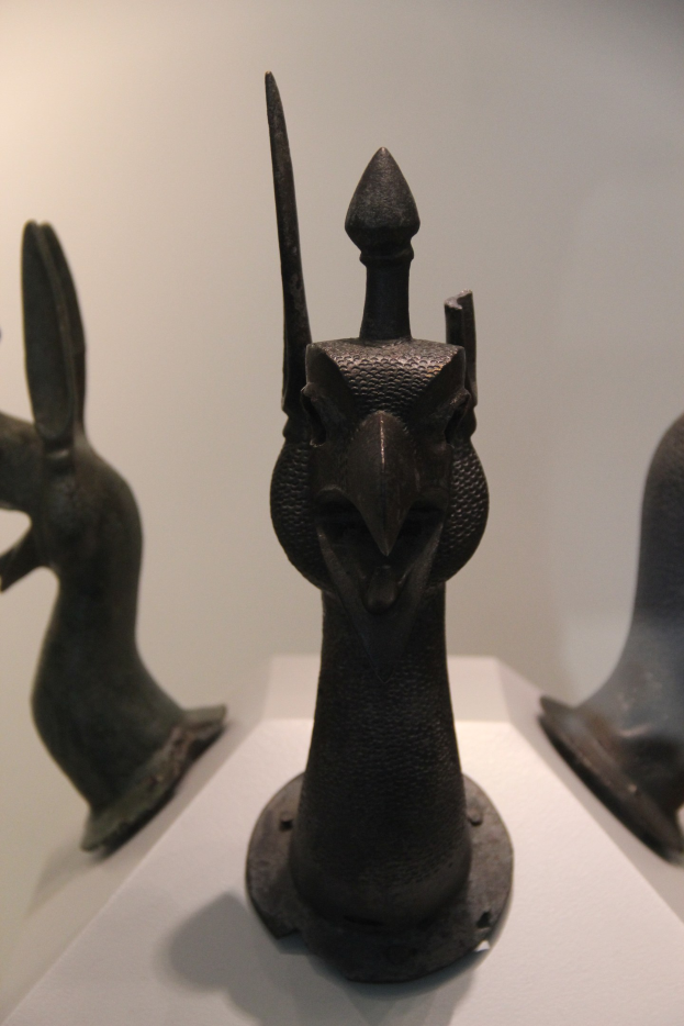 Drei Bronzeplastiken auf einer wei├čen Unterlage in einem Museum mit einer Wand im Hintergrund.