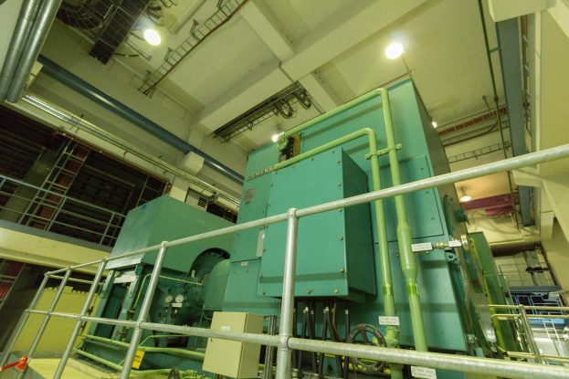 Großer industrieller Wärmetauscher in einem Gebäude umgeben von Geländern, Rohren, Ventilen und Beleuchtung.