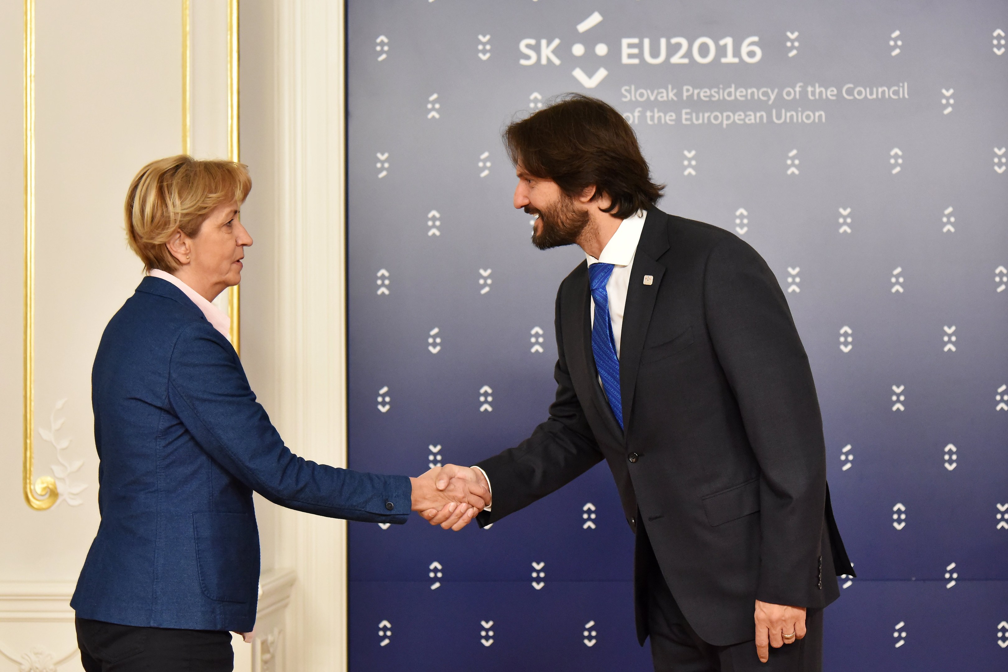 Bundeskanzlerin Angela Merkel und Bundespräsident Joachim Gauck schütteln sich vor einem 'EU-Gipfel'-Plakat die Hände und lächeln freundlich.