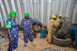 Eine Gruppe von Männern steht um einen Reifenhaufen, einer hält einen Reifen, mit einer Maschine rechts und Metallplatten im Hintergrund, die wie ein Reifenreparaturteam aussehen.