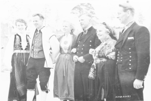 Eine Gruppe von Menschen in den 1930er Jahren, die zusammen draußen stehen, lächeln und Bäume im Hintergrund haben, mit dem Text "Bayerische Familie in den 1930er Jahren" unten.