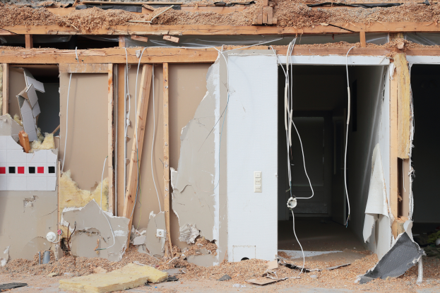 Ein abgerissenes Haus mit verstreuten Wänden, Holzstücken, Drähten und anderem Schutt auf dem Boden.