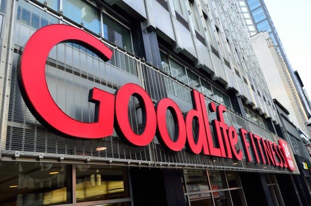 Außenansicht eines Goodlife Fitness Studios in New York City mit Glaswänden, einem Namensschild, benachbarten Gebäuden auf der rechten Seite und Himmel im Hintergrund.
