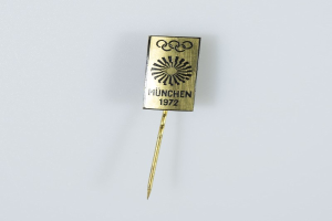 Goldene Nadel mit «München 1972 Olympische Spiele» Text auf weißem Hintergrund.