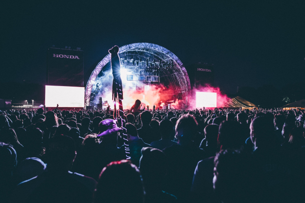 Eine große Menge bei einem Musikfestival mit einem Künstler auf einer beleuchteten Bühne umgeben von Bildschirmen und Bannern.