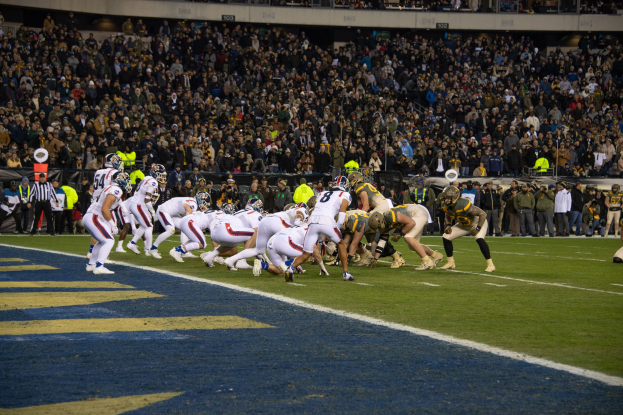 Fußballspieler in Sportkleidung und Helmen liegen während eines Spiels in einem Stadion mit Zuschauern und Tafeln im Hintergrund.