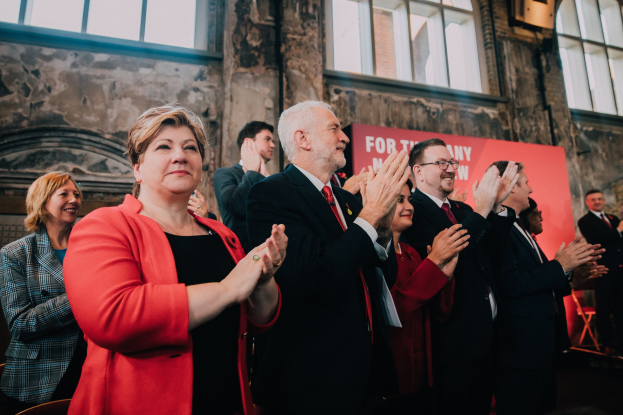 Gruppe von Menschen, die vor einer Menge klatschen, mit einem Banner im Hintergrund, auf dem "Wahlsieg" zu lesen ist.