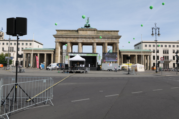 Das Brandenburgische Tor in Berlin, Deutschland, mit seinen ikonischen Säulen und Statuen, umgeben von Gebäuden, Laternenmasten, Ampeln, Zelten, Fahrzeugen, Menschen, Fahrrädern und grünen Ballons am Himmel während des Berlin-Marathons.