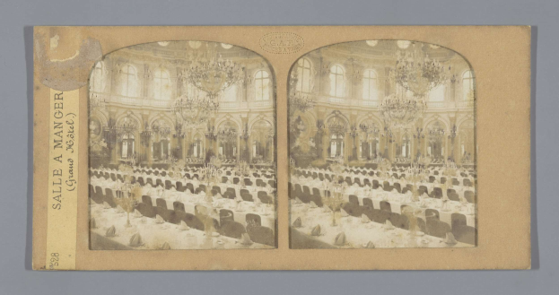 Ein altes Foto eines prächtigen Hotel-Speisesaals mit üppigen Kronleuchtern, langen Tischen mit Stühlen und großen Fenstern, auf dem links ein Schild mit der Aufschrift "Sale à Manger, Grand Hotel" zu sehen ist.