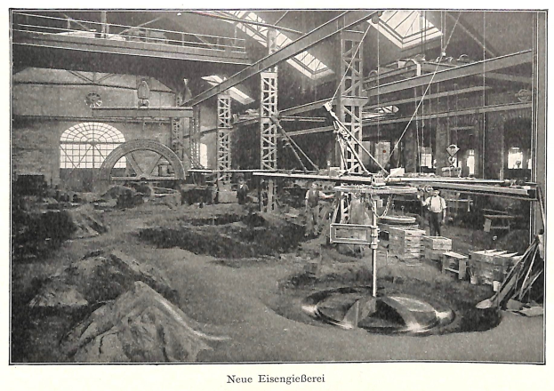 Schwarzes und weiße Foto eines Fabrikinneren mit Arbeitern, die Maschinen bedienen, umgeben von Metallstangen und -pölen, beschriftet mit "Neue Eisenglebeerei, die erste Fabrik in Deutschland" unten.