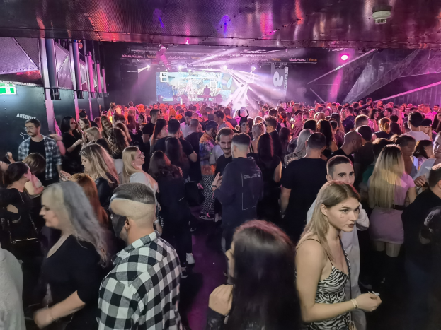 Eine große Gruppe von Menschen in einem hell erleuchteten Nachtclub mit Deckenlichtern und Säulen bei einem Absolut Nightlife-Event.