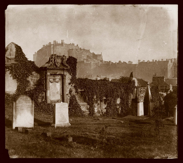Altes Schwarz-Weiß-Foto eines Friedhofs mit Grabsteinen und Efeu im Vordergrund, einem Schloss im Hintergrund und Gebäuden und Himmel oben.