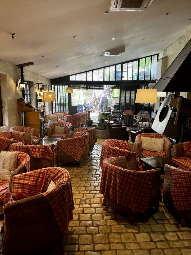 Ein geräumiges Hotelfoyer mit Reihen von Stühlen und Tischen, gepolsterten Sofas, an der Wand montierten Lampen, einer Deckenklimaanlage und Glasfenstern im Hintergrund.
